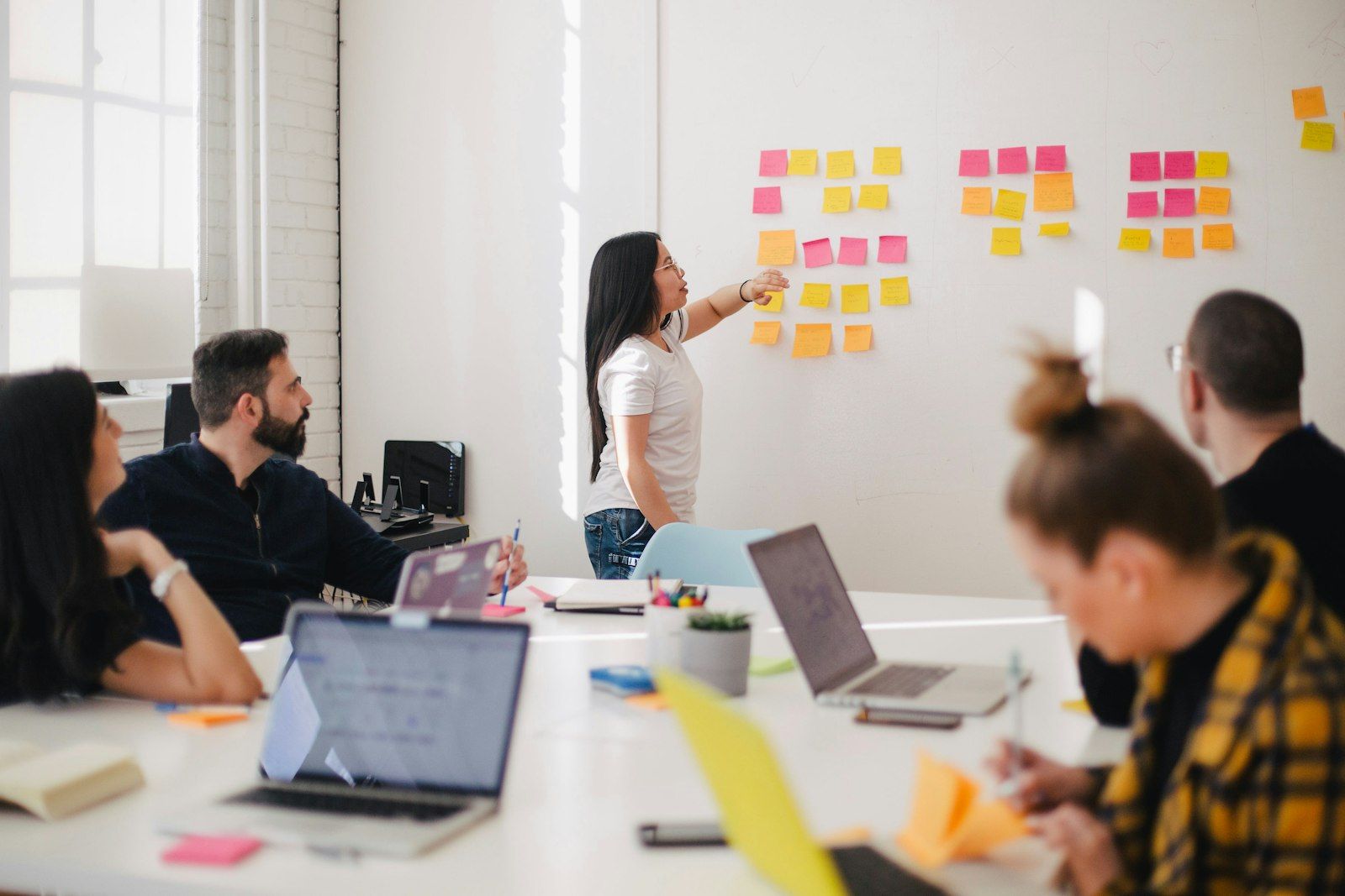 Colleagues at a table while one person points at sticky notes on a whiteboard